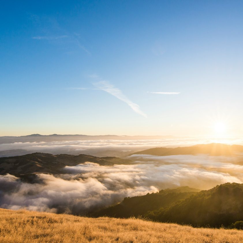 Sunlight breaking over a sea of clouds above the California hills